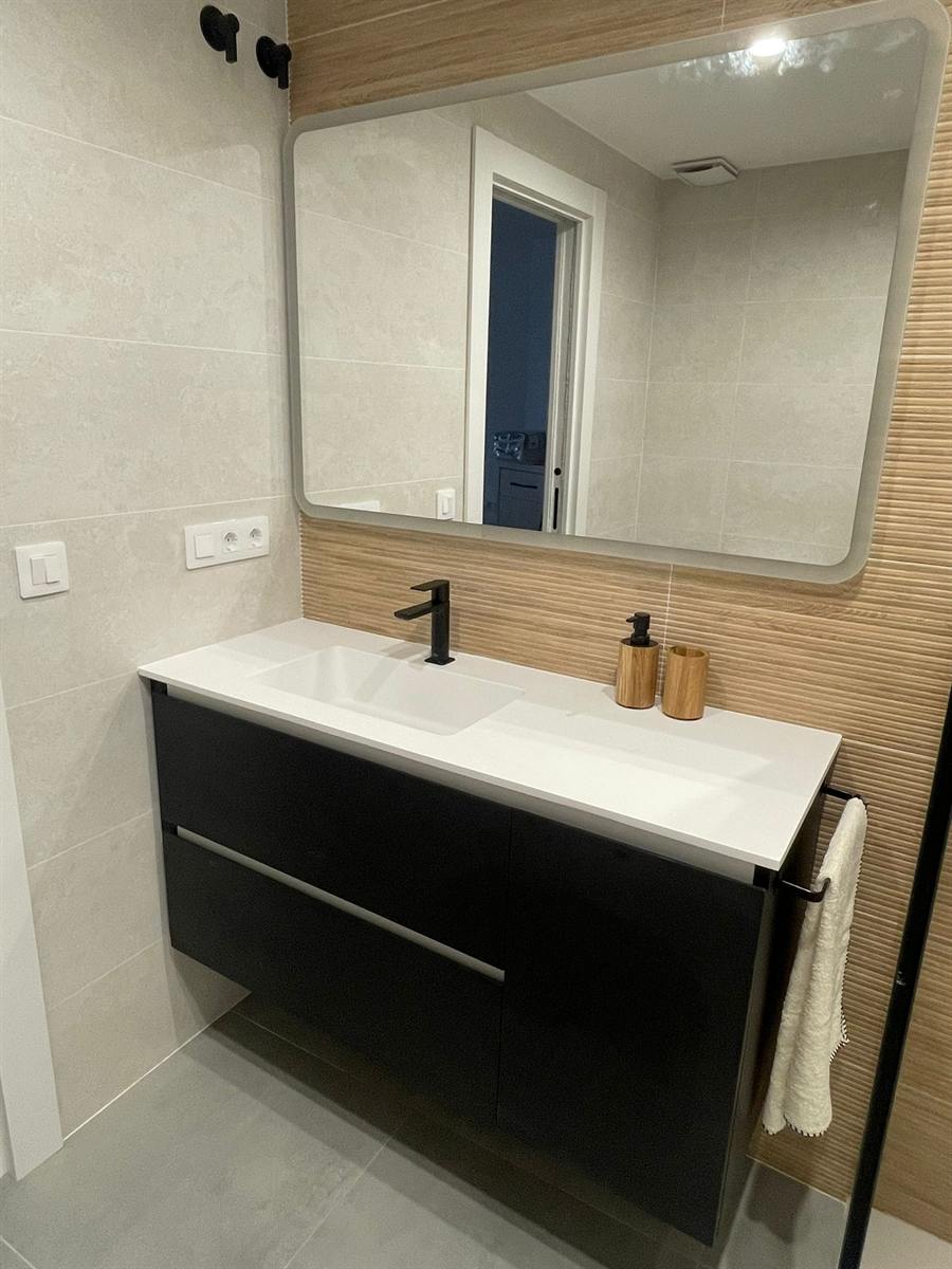 Baño con mueble negro, encimera blanca y espejo retroiluminado