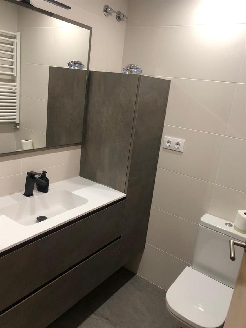 Baño con mueble en tono cálido, espejo con luz y toallero