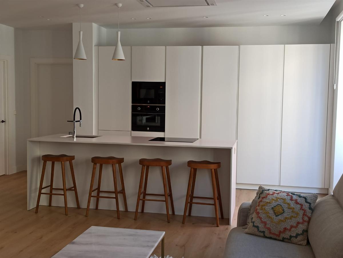 Cocina blanca en isla abierta al salón, con taburetes de madera